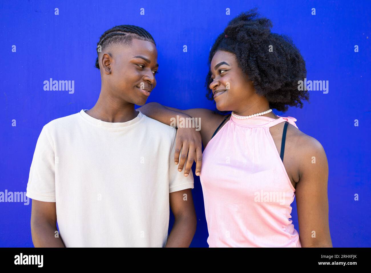Positif jeune couple afro-américain dans des vêtements décontractés avec coiffure afro et tresse se penchant ensemble sur fond bleu et regardant chacun OT Banque D'Images