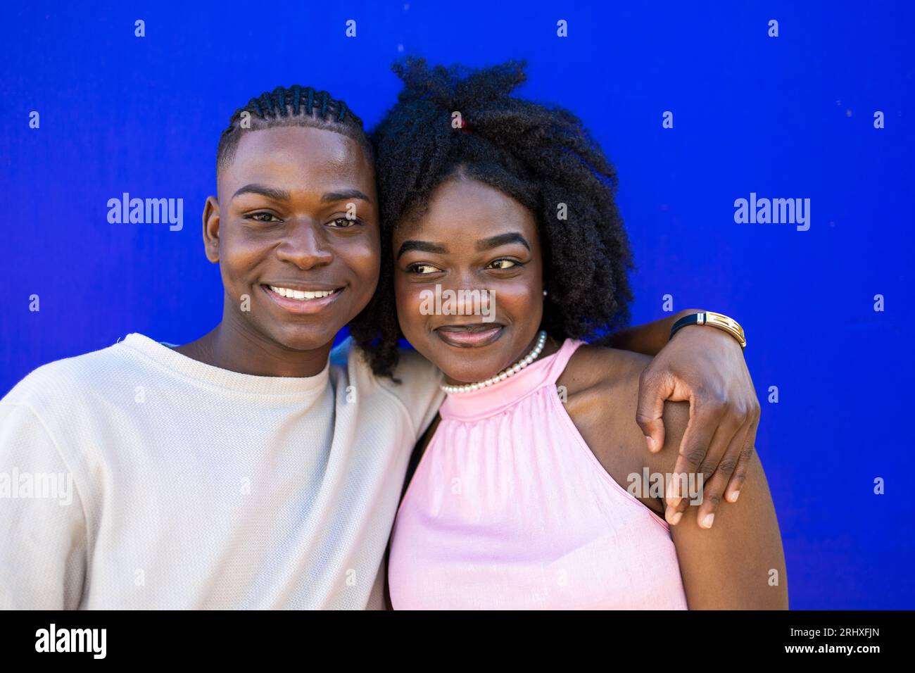 Positif jeune couple afro-américain dans des vêtements décontractés avec coiffure afro et tresse se penchant ensemble sur fond bleu et regardant la caméra Banque D'Images