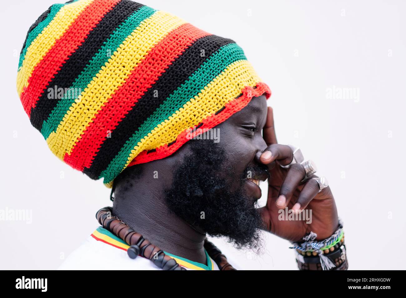Vue latérale de l'homme afro-américain dans le chapeau coloré debout et regardant loin tout en touchant le visage sur fond blanc Banque D'Images