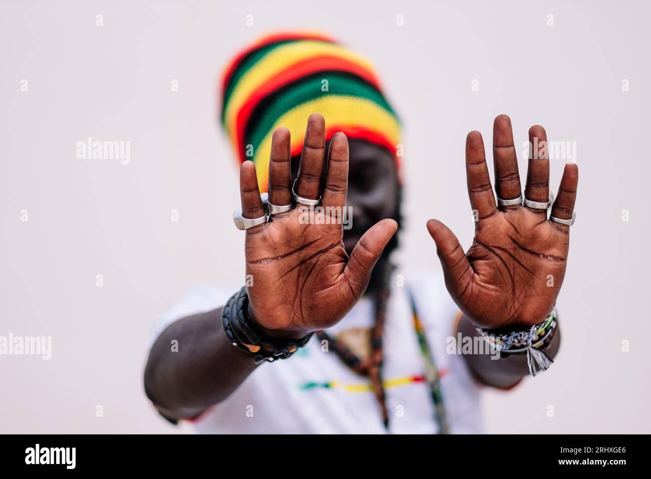 Homme afro-américain flou dans le chapeau coloré debout et regardant la caméra tout en mettant les mains devant la caméra sur fond blanc Banque D'Images