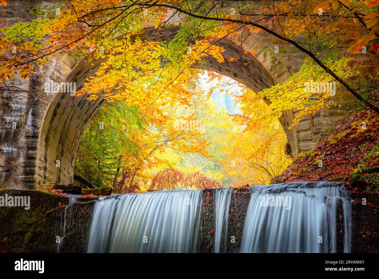 Fantastique paysage d'automne d'automne - cascade de rivière dans le parc forestier d'automne coloré avec des feuilles rouges jaunes avec vieux pont, fond de papier peint Banque D'Images