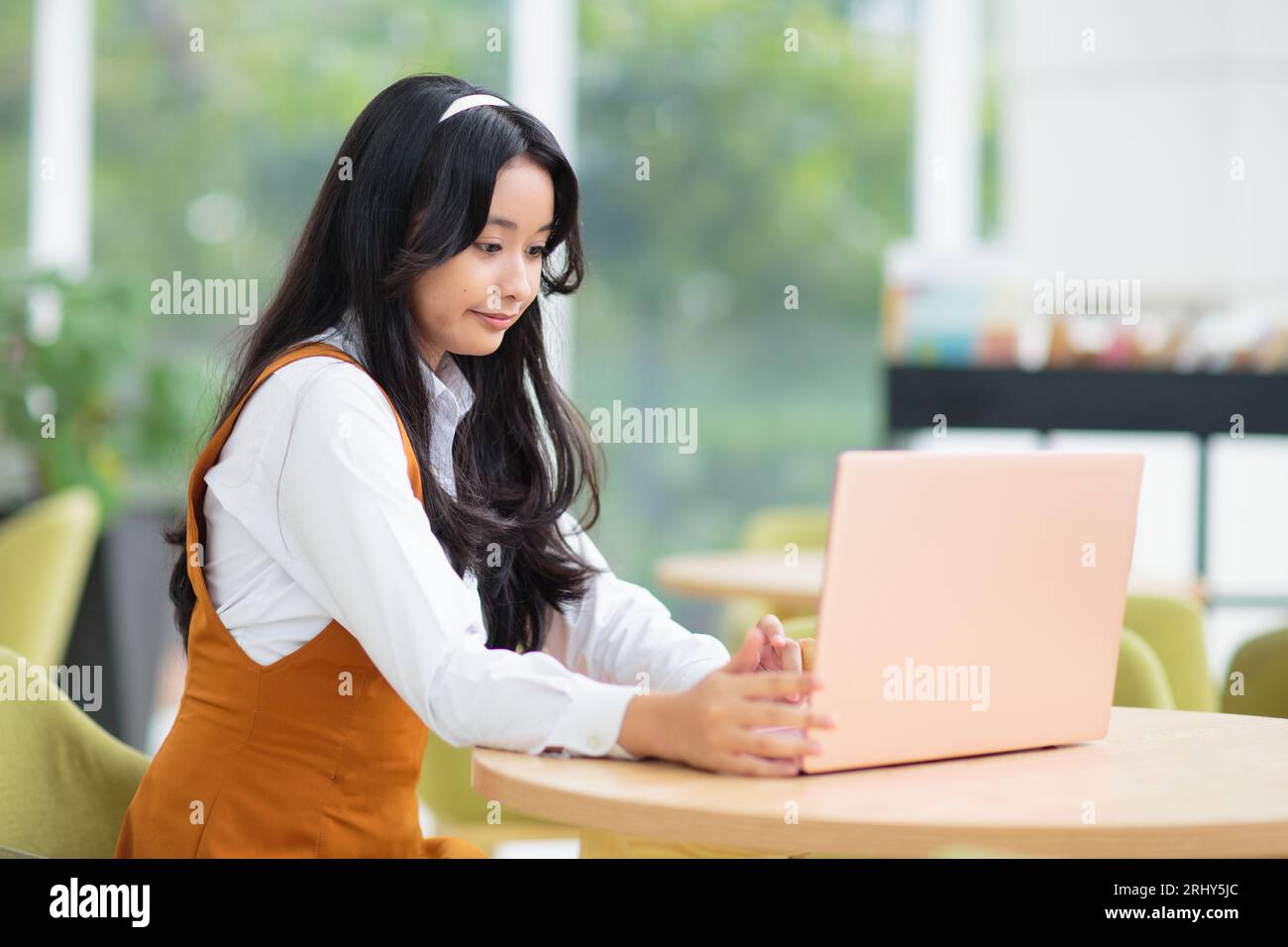 Belle adolescente asiatique avec ordinateur portable. Jeune femme avec les cheveux longs travaillant sur l'ordinateur dans le restaurant. Étudiant faisant ses devoirs. Banque D'Images