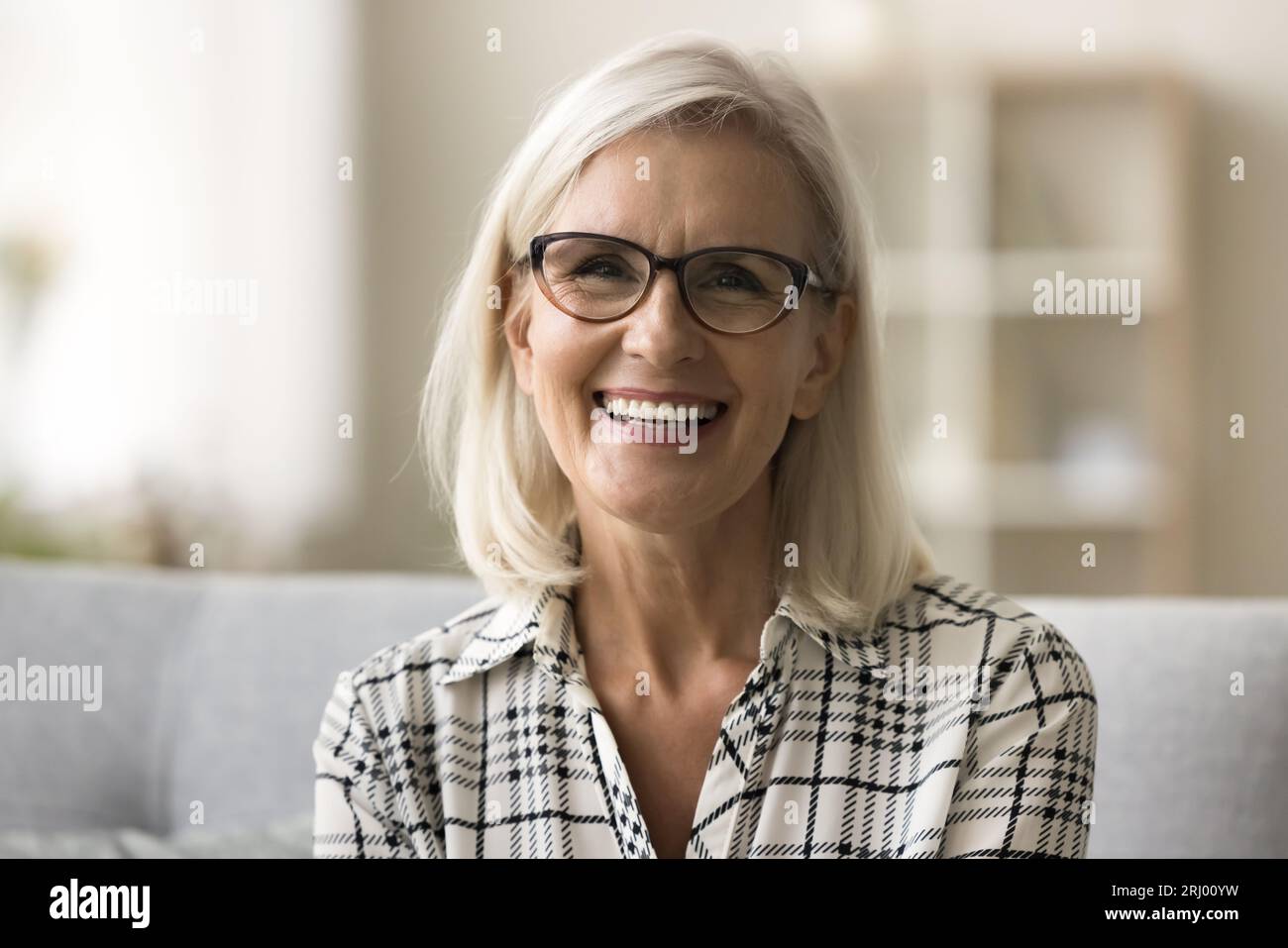Femme mûre blonde joyeuse dans des lunettes à la mode et chemise décontractée Banque D'Images