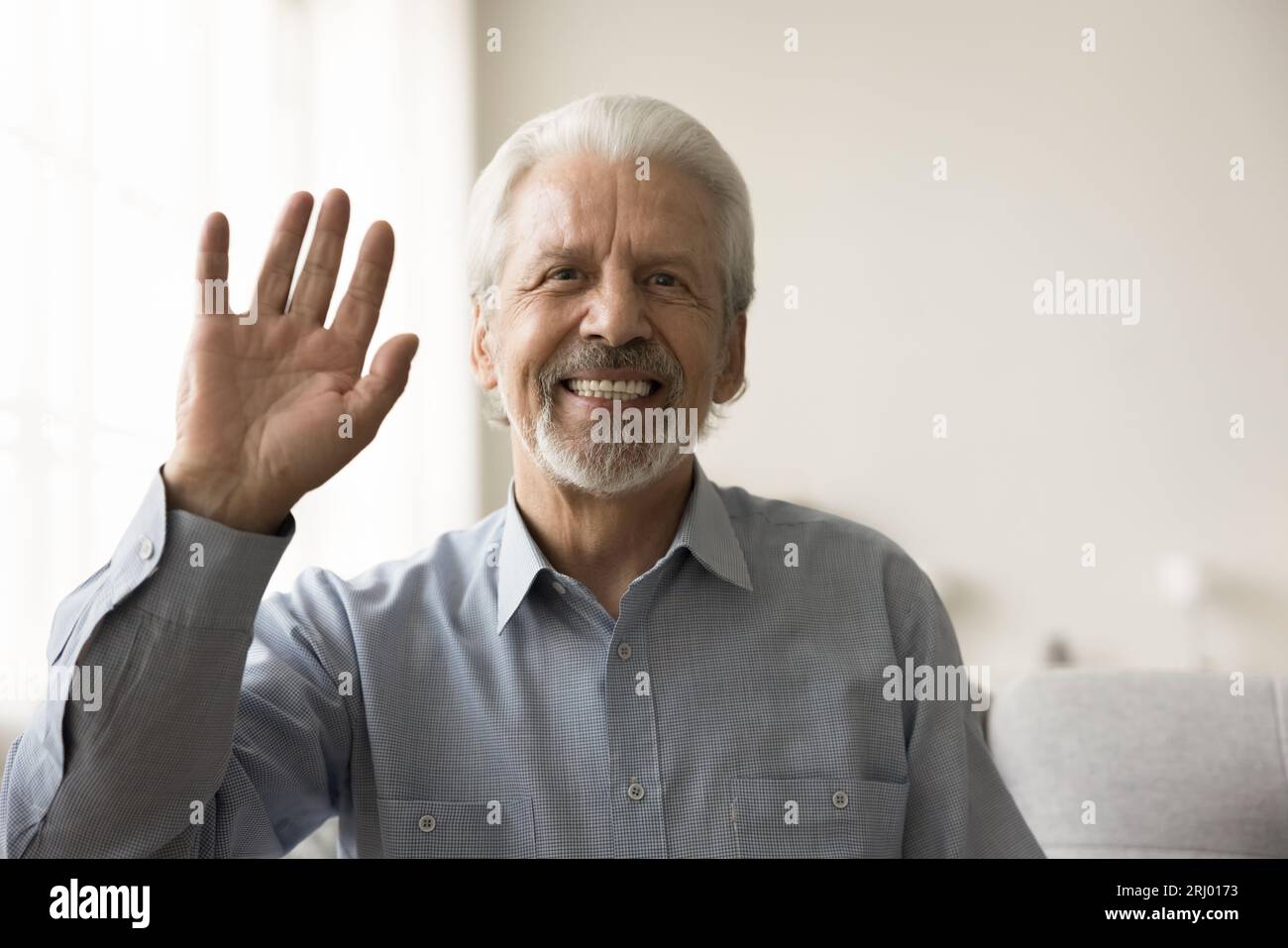 Joyeux vieux retraité homme des années 70 agitant la main bonjour à la caméra Banque D'Images
