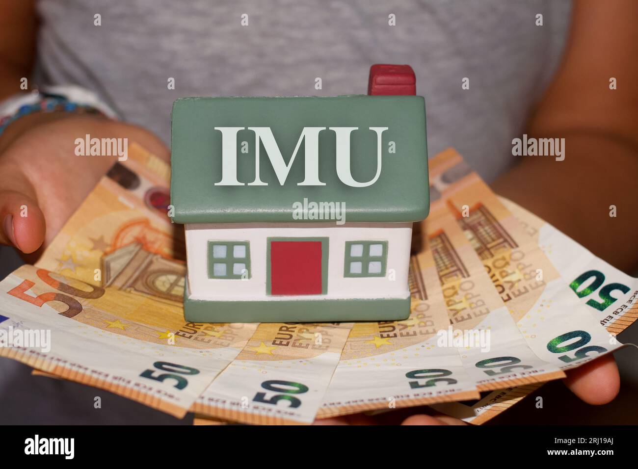 Personne détenant une maison avec des billets en euros avec le signe «IMU» taxe italienne Banque D'Images