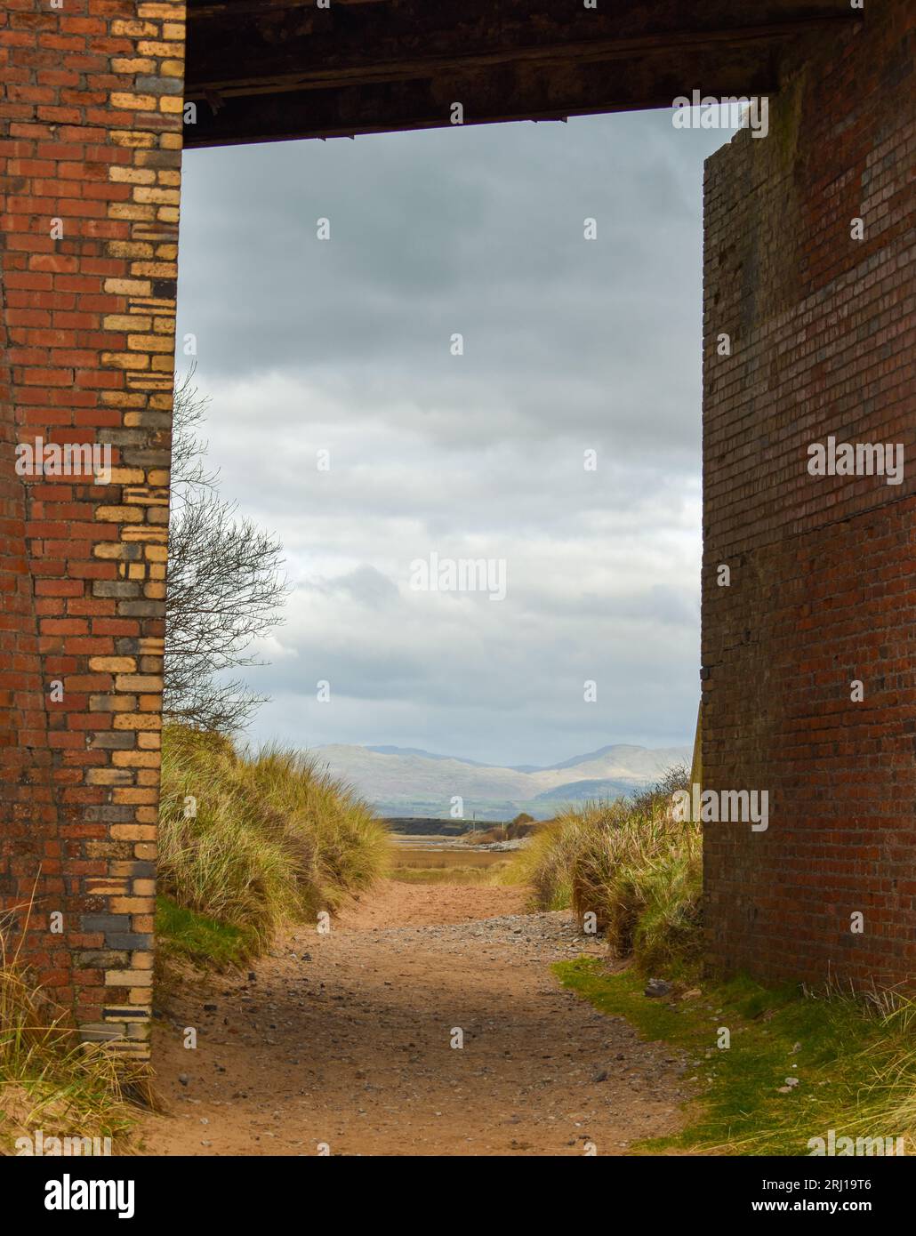 La vue sous un vieux pont de briques sur une plage avec les pics du Lake District légèrement visibles au loin. Banque D'Images