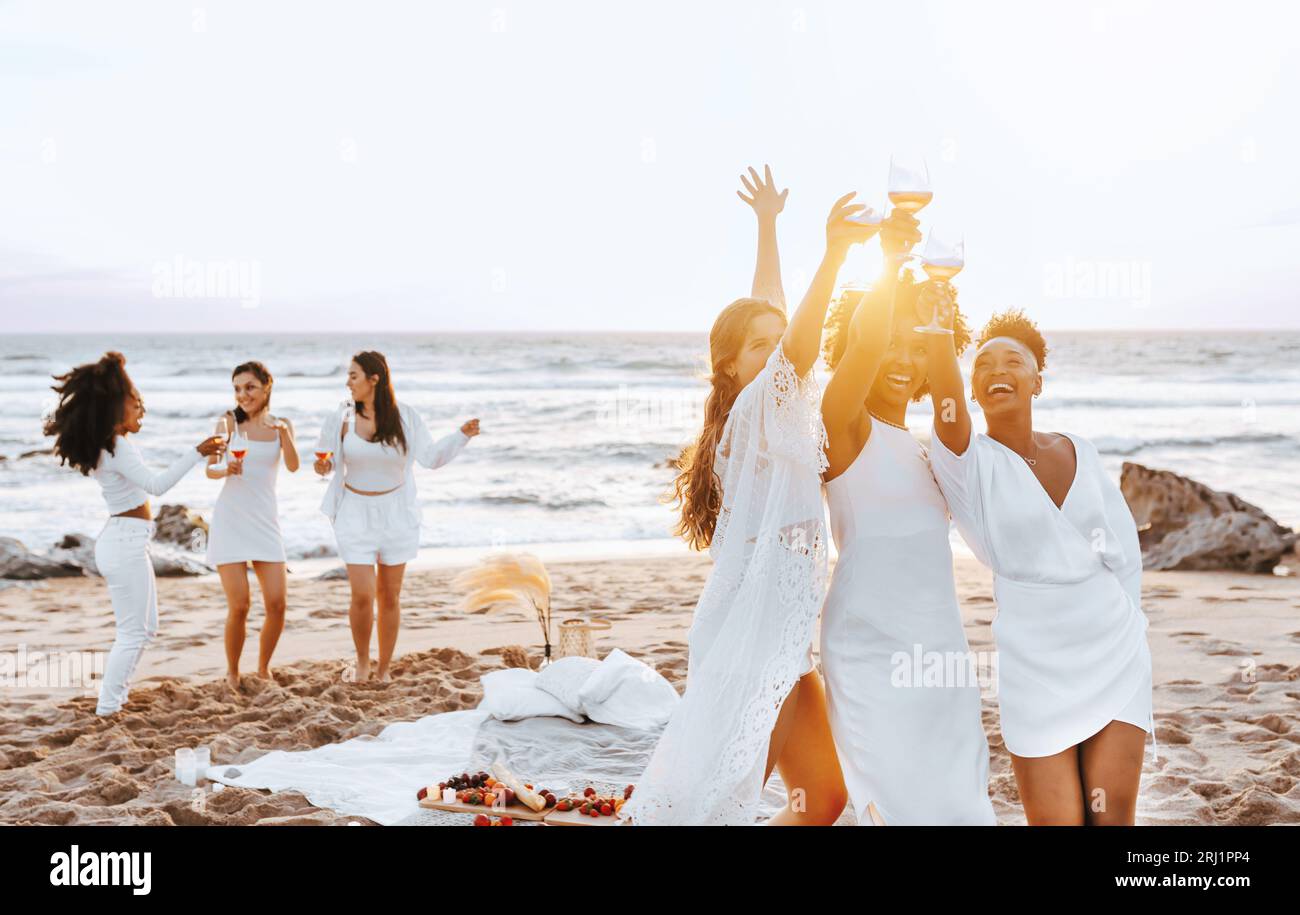 Les femmes insouciantes marient l'équipe de grillage de verres à vin tout en ayant une fête de poule et en dansant sur la plage au bord de la côte Banque D'Images