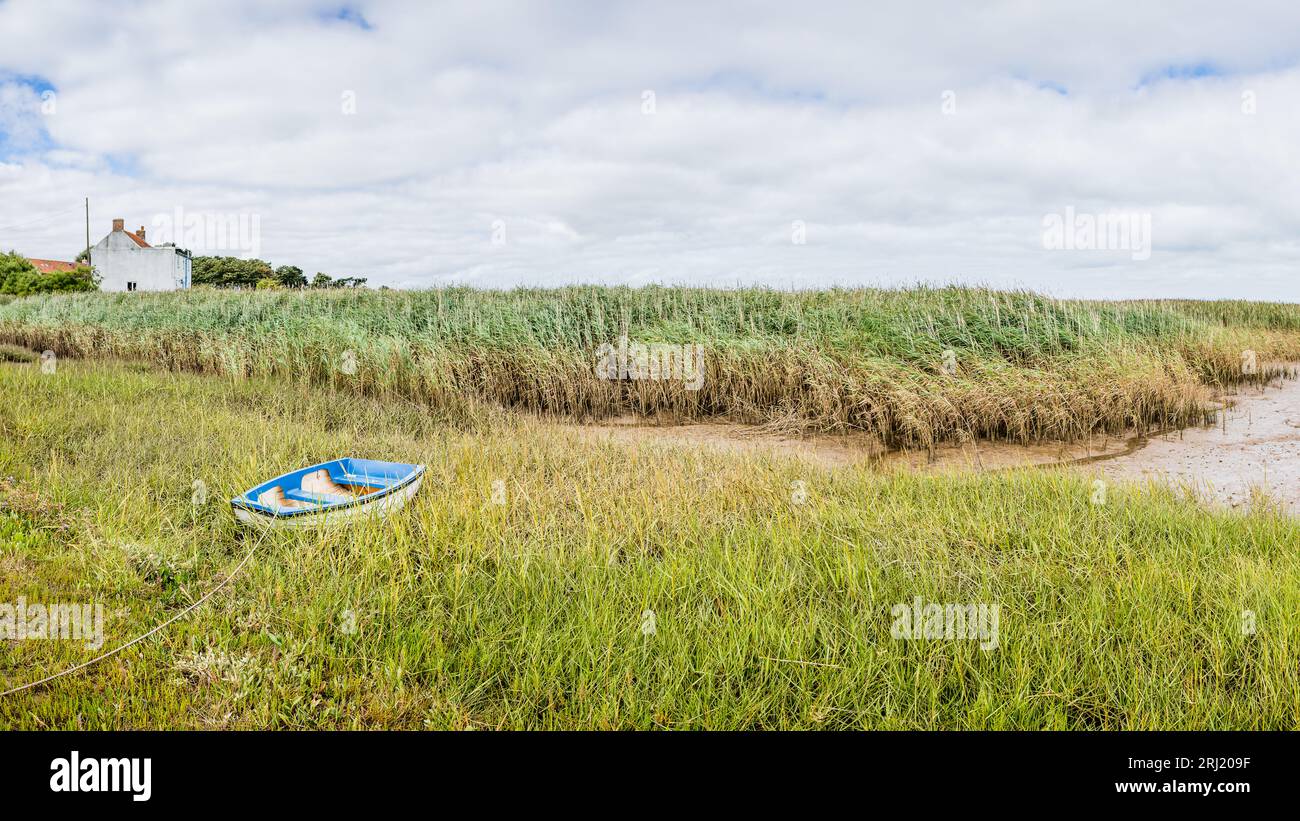 Un panorama multi-images d'un bateau solitaire attaché au rivage à Brancaster Staithe et assis sur de longues herbes à marée basse sur la côte nord de Norfolk. Banque D'Images