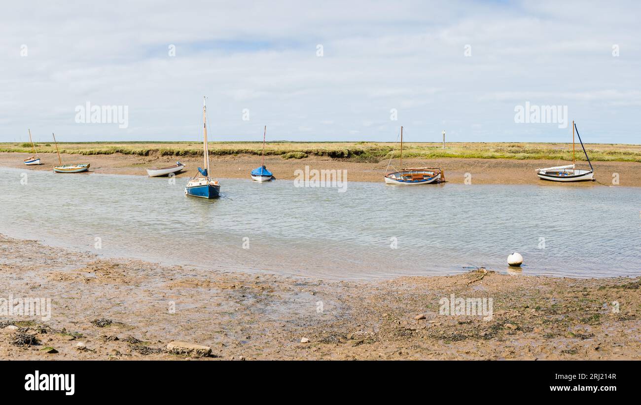 Petits bateaux à Burnham Overy Staithe vus à marée basse entre les marais et vasières sur la côte nord du Norfolk en août 2023. Banque D'Images