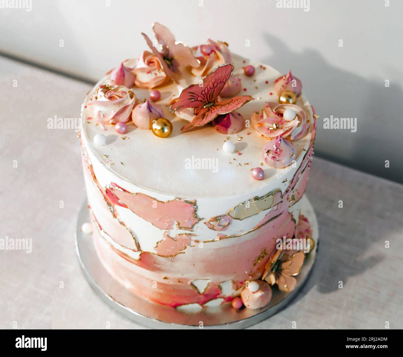 Gâteau d'anniversaire décoré avec des fleurs de sucre rose et des papillons. Banque D'Images