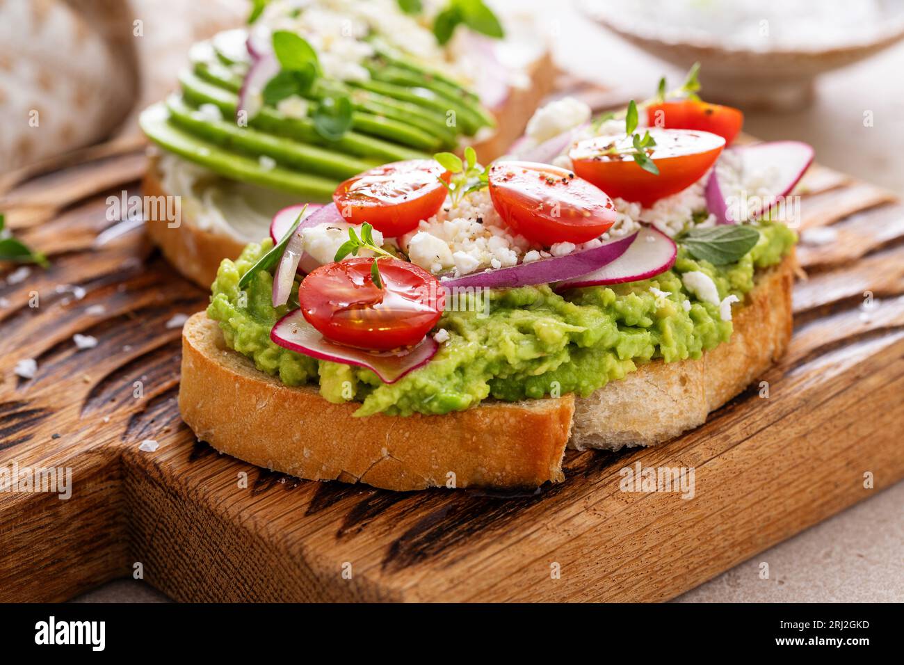 Toasts d'avocat avec radis, tomates et feta garnis d'huile d'olive, idée de petit déjeuner sain Banque D'Images