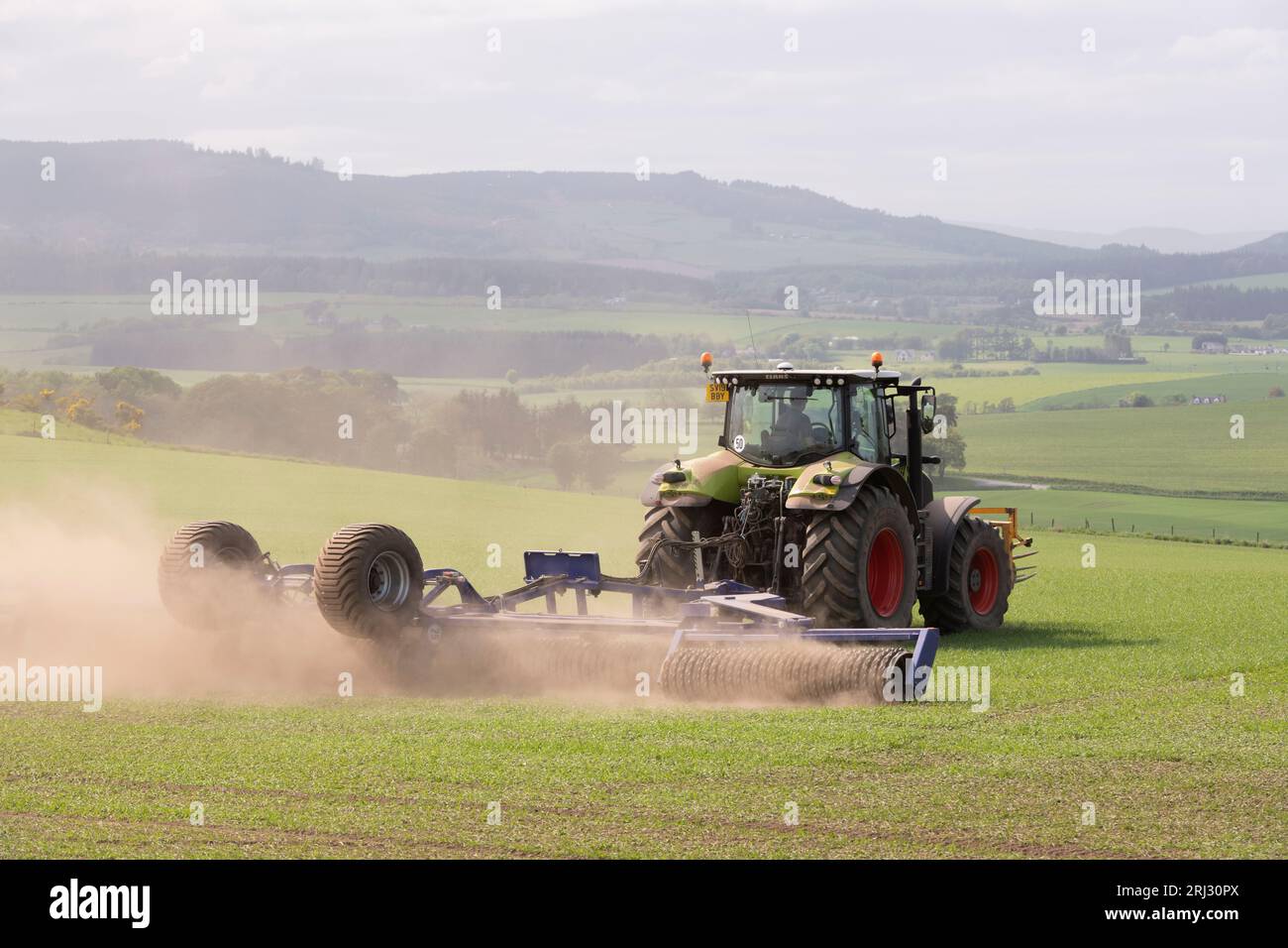 Un tracteur Claas avec Dal-Bo Power Roll 1530 Rolling un champ d'orge de printemps avec vue sur la campagne environnante de l'Aberdeenshire Banque D'Images