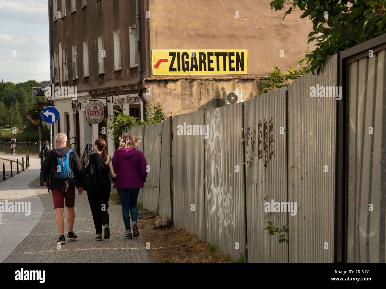 Zgorzelec, Pologne. 08 août 2023. 08.08.2023, Zgorzelec. Un panneau sur un pare-feu annonce l'achat de cigarettes dans un magasin de Zgorzelec, qui est situé à une centaine de mètres derrière la frontière germano-polonaise, un pont de la ville. Les touristes marchent à côté du panneau. Zgorzelec est le voisin polonais de la ville allemande de Goerlitz, sur l'autre rive de la rivière Neisse. Les cigarettes et l'alcool sont moins chers ici qu'en Allemagne. Crédit : Wolfram Steinberg/dpa crédit : Wolfram Steinberg/dpa/Alamy Live News Banque D'Images