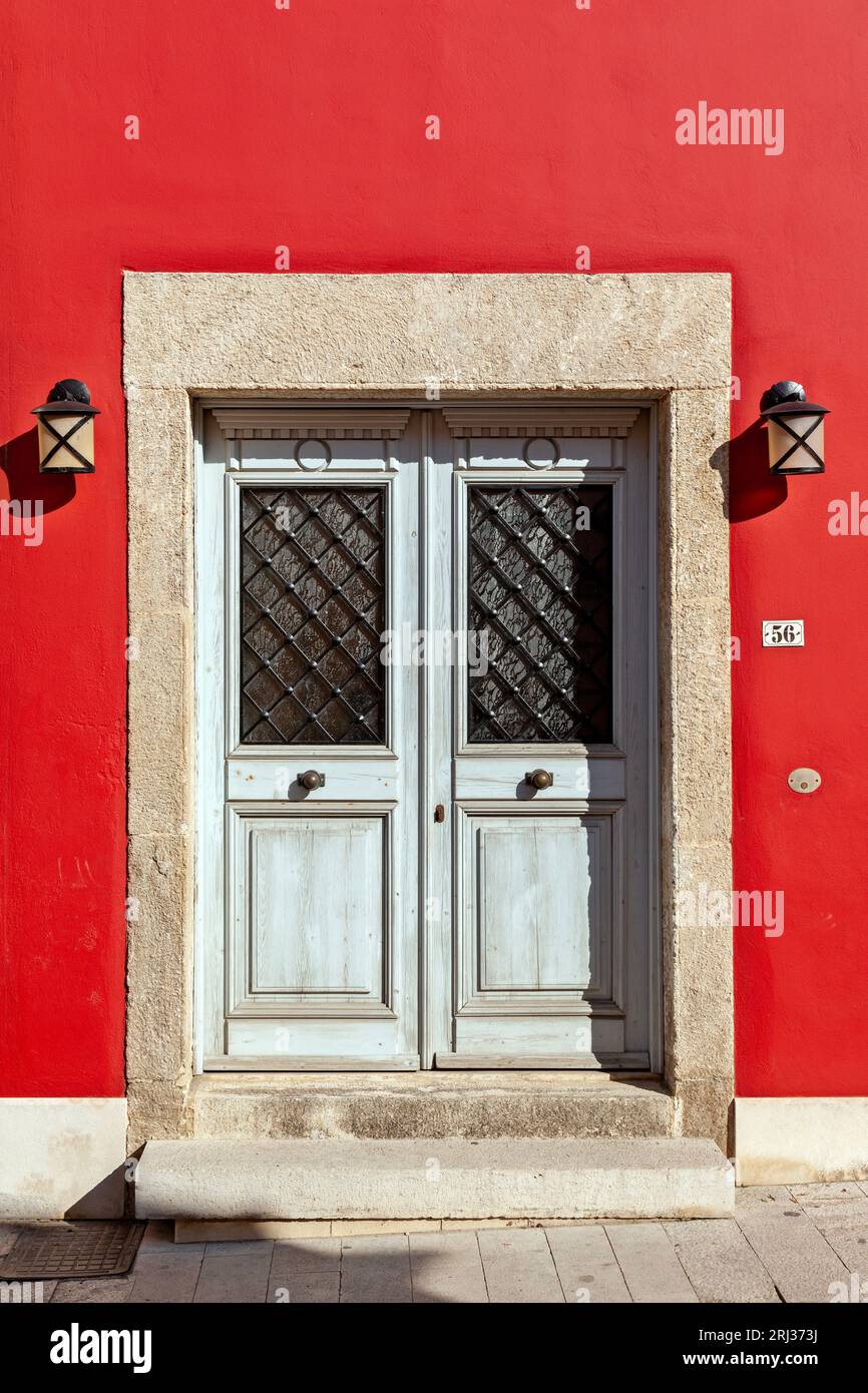 Incroyable entrée traditionnelle en bois avec portes doubles, deux lumières latérales et linteau en pierre et seuil, et un mur rouge vif, en Crète. Banque D'Images