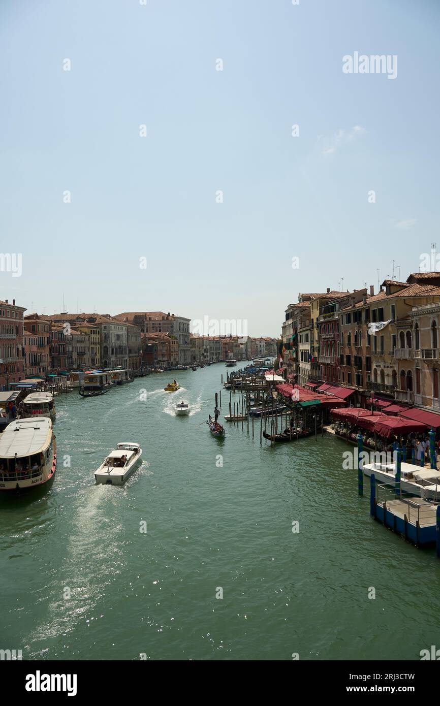 Une vue sur une rivière à Venise, en Italie, avec plusieurs bateaux de différentes tailles et couleurs, naviguant le long de l'eau calme et bleue Banque D'Images