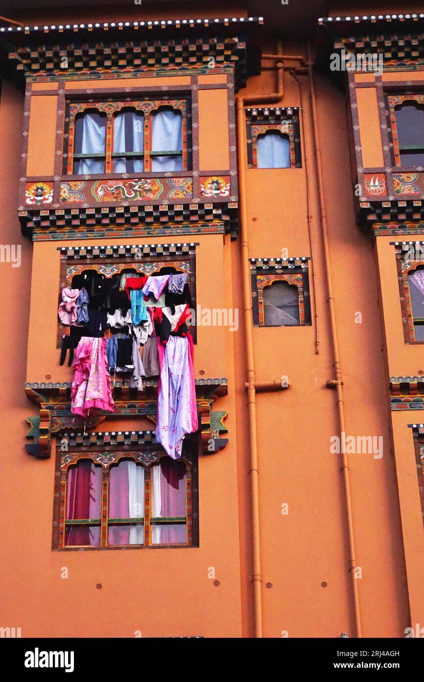 Des vêtements colorés pendent à l'extérieur d'une banque de fenêtres de rabats sur un bâtiment orange avec des décorations traditionnelles peintes à Paro, Royaume du Bhoutan. Banque D'Images