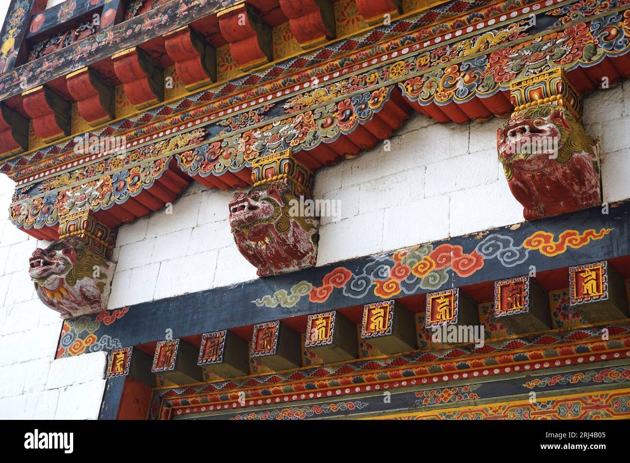 Les têtes sculptées et peintes ressortent du mur blanc au-dessus et en dessous des boiseries traditionnelles finement décorées à Punakha Dzong, Royaume du Bhoutan. Banque D'Images