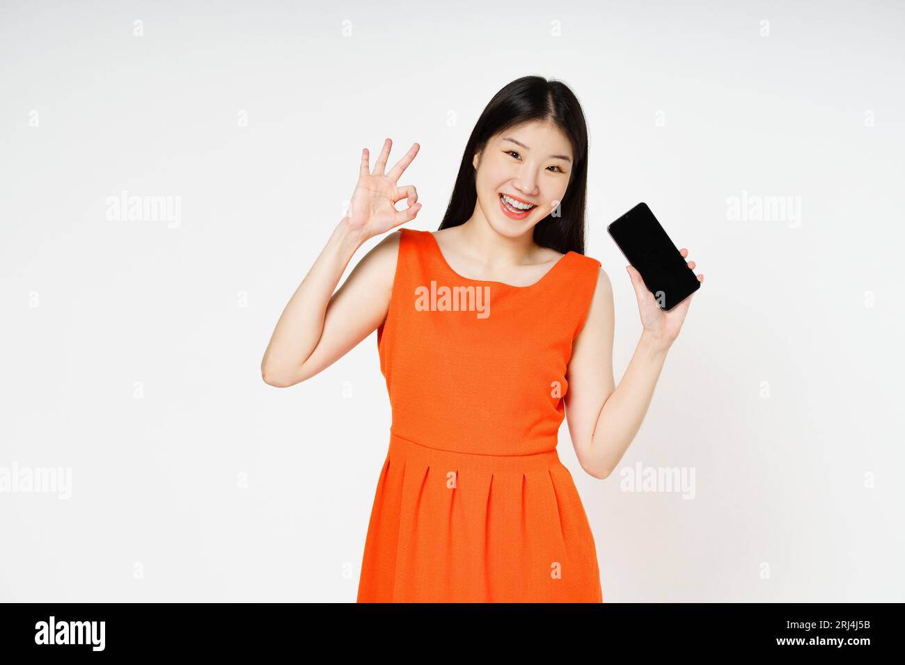 Jeune femme tenant un smartphone et affiche le signe OK sur fond blanc. Banque D'Images