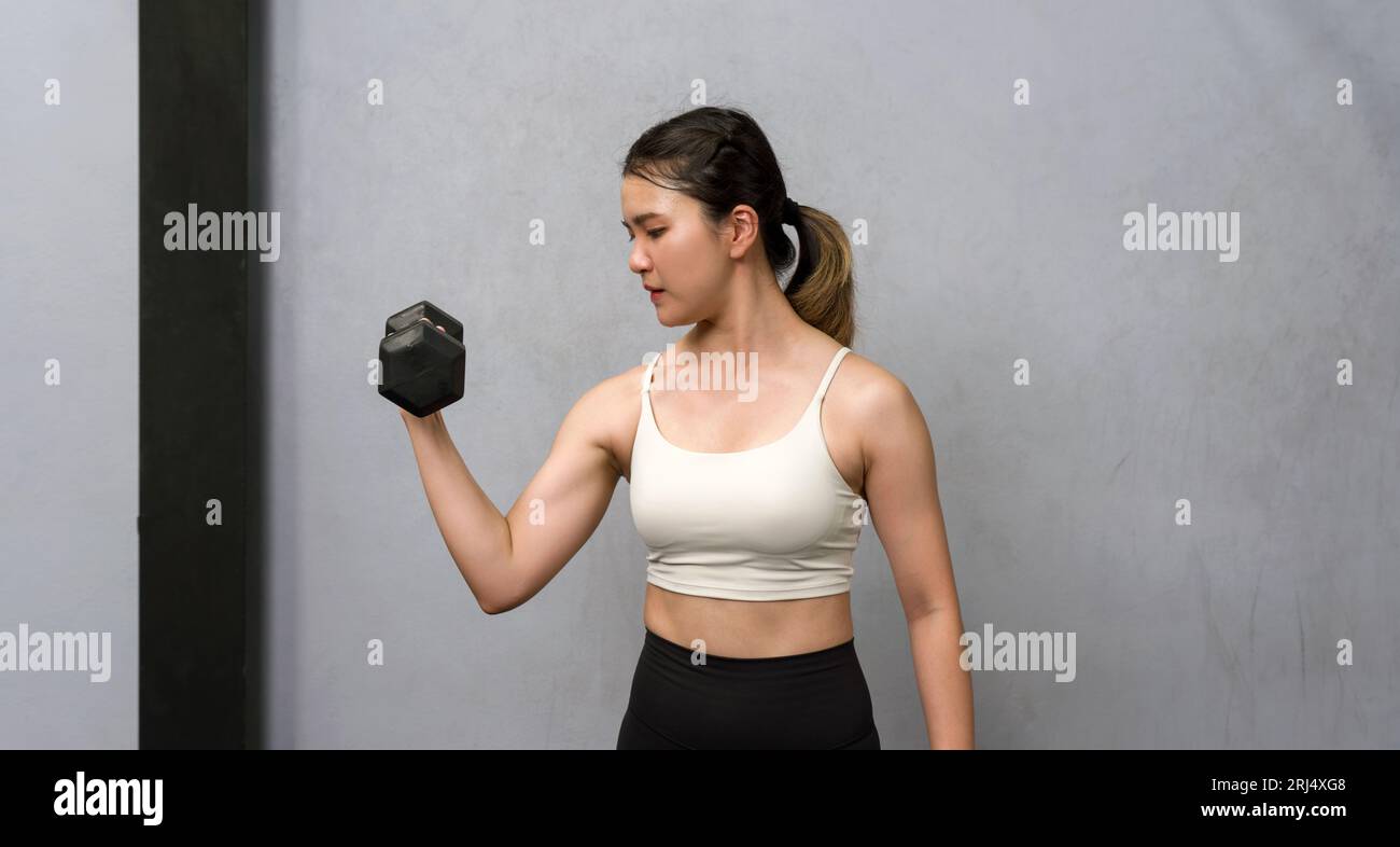 Une femme en forme physique engagée dans une séance d'entraînement dans une salle de gym moderne, soulevant avec détermination un haltère lourd alors qu'elle s'efforce de la force et du bien-être. Banque D'Images