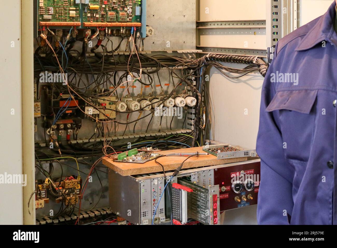 Un électricien de travail masculin se tient devant un panneau électrique avec des fils, des transistors, des fusibles, des composants électroniques et des commutateurs. Banque D'Images