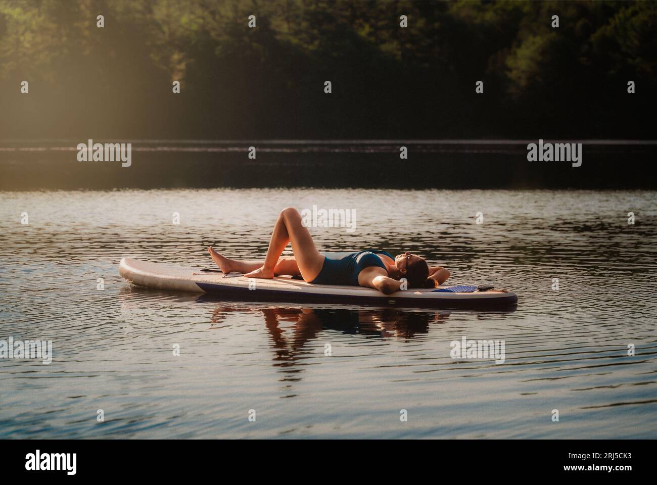 Femme en maillot de bain couché sur stand up paddleboard sur le lac. Banque D'Images