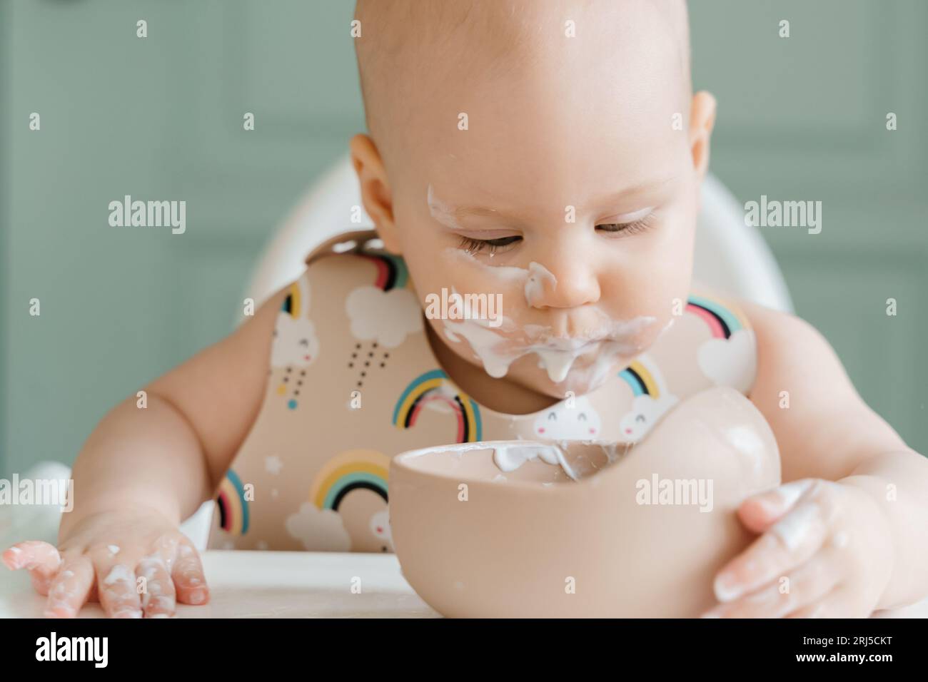 Un joli bébé taché de nourriture âgé d'un demi-an mange du yaourt assis Banque D'Images