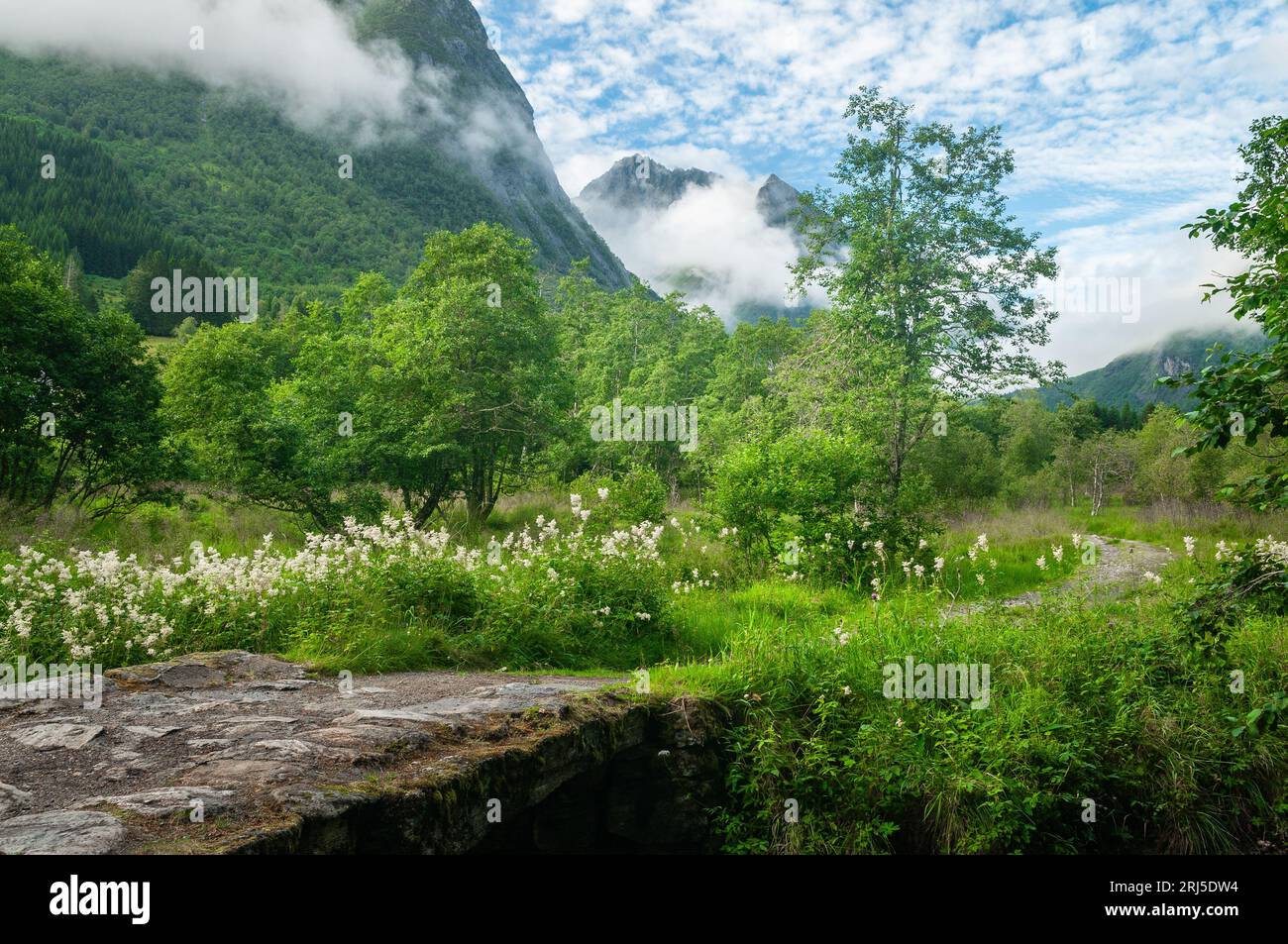 vieux pont sur un ruisseau avec un chemin vers la montagne qui surgit des nuages arrière Banque D'Images