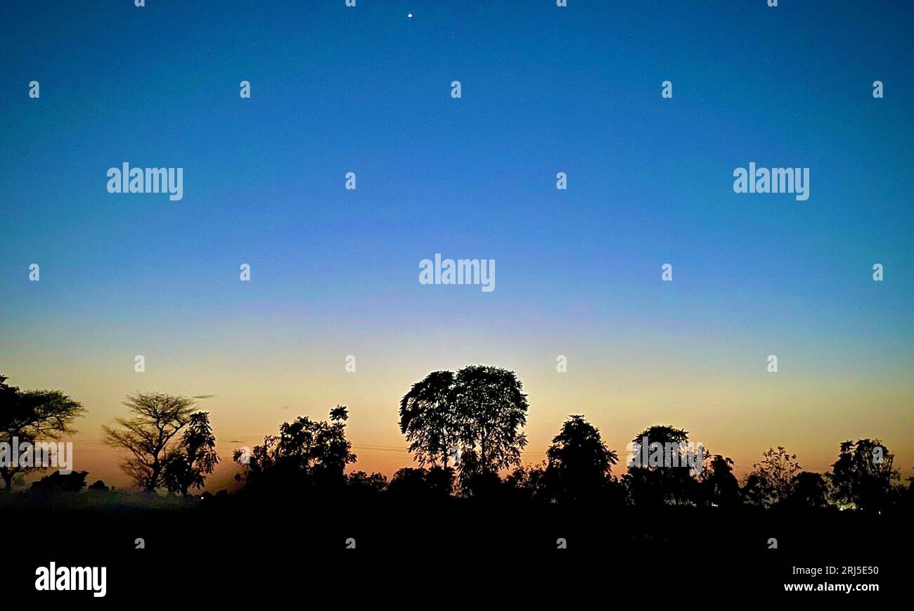 Un paysage idyllique en début de soirée avec une scène tranquille bordée d'arbres et un croissant de lune doré dans le ciel Banque D'Images