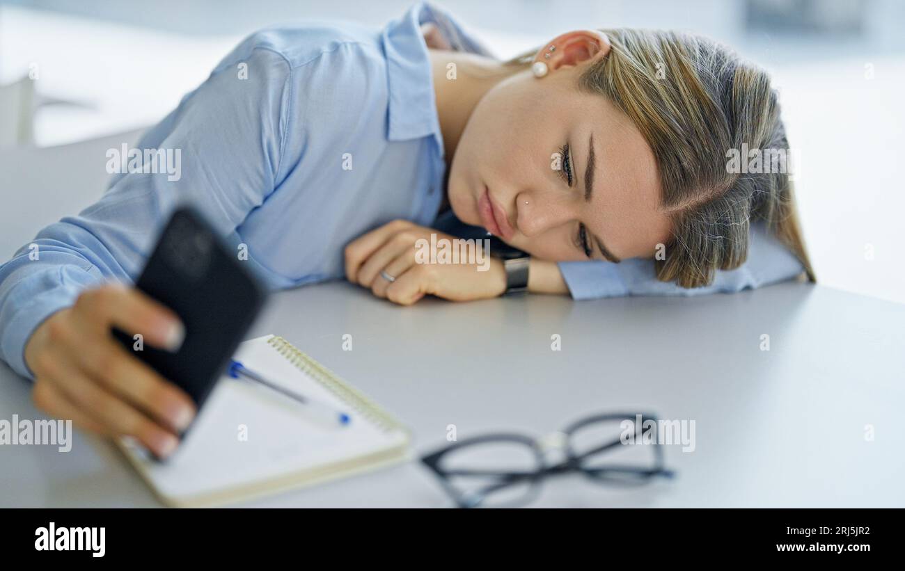 Jeune femme blonde étudiant utilisant smartphone fatigué au bureau Banque D'Images