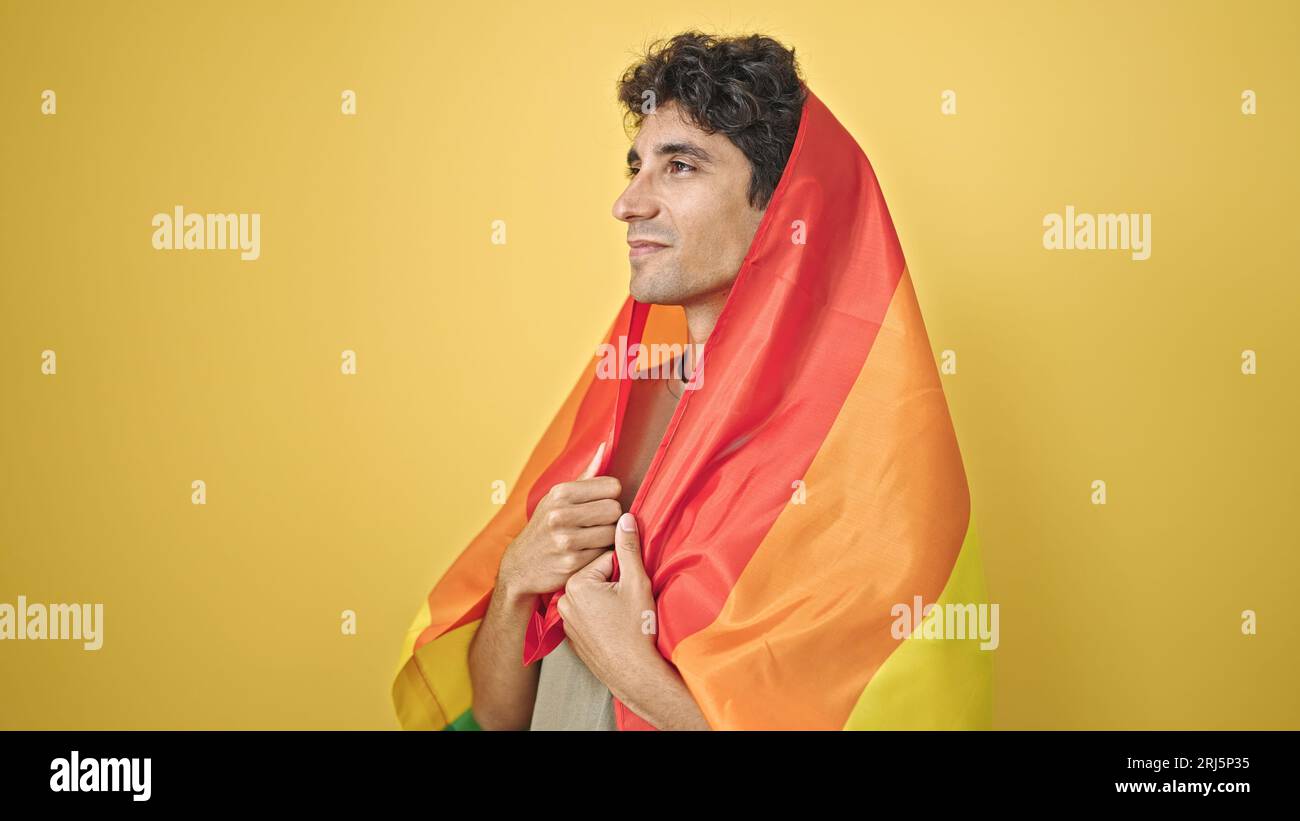Jeune homme hispanique portant le drapeau arc-en-ciel avec une expression détendue sur fond jaune isolé Banque D'Images