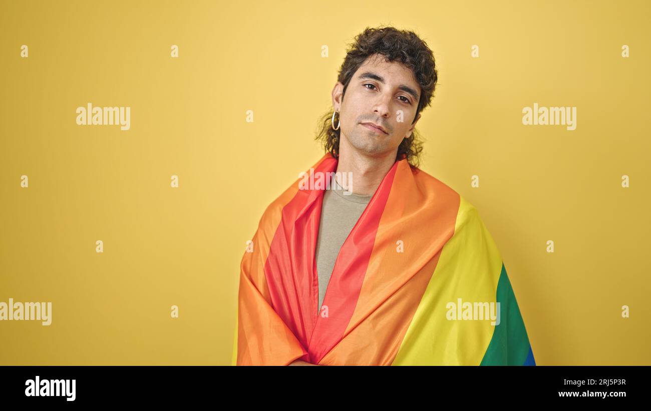 Jeune homme hispanique portant le drapeau arc-en-ciel avec une expression détendue sur fond jaune isolé Banque D'Images