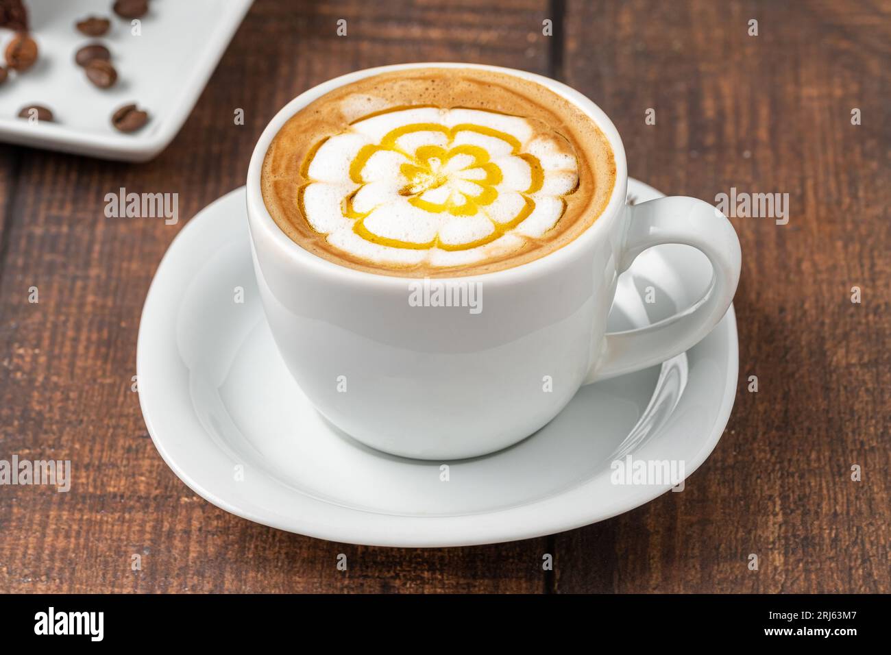 Café cappuccino à motifs dans une tasse en porcelaine blanche sur une table en bois Banque D'Images