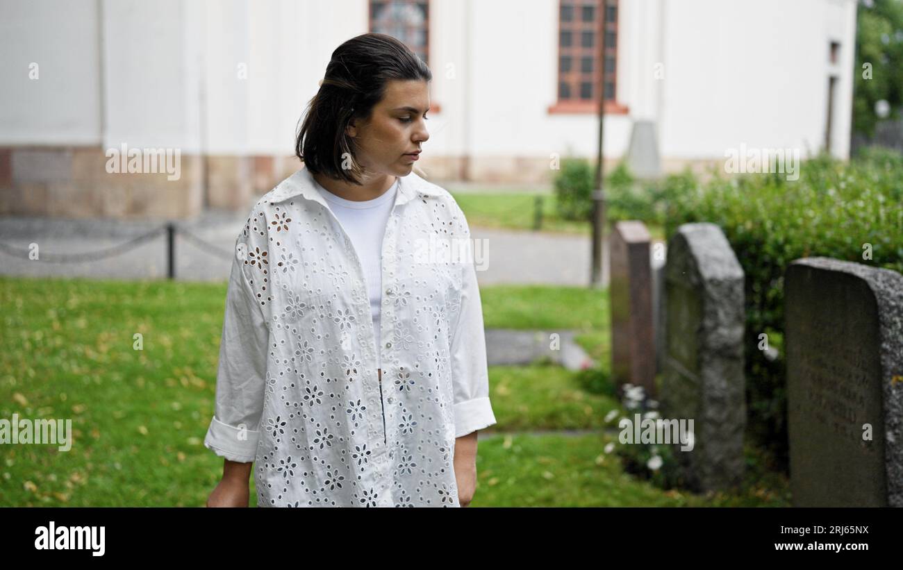 Belle jeune femme hispanique marchant par les pierres tombales au cimetière Banque D'Images