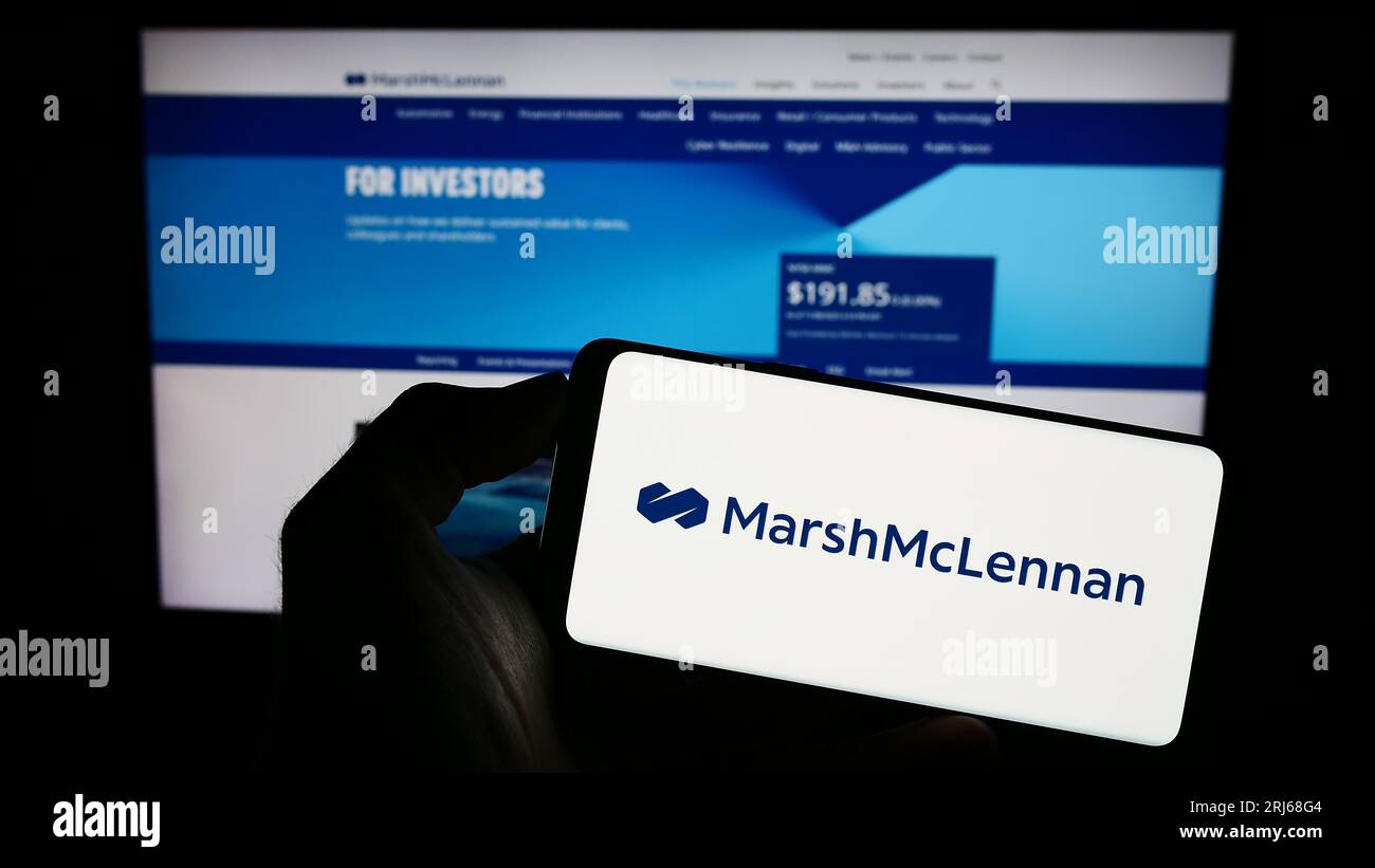 Personne tenant un téléphone mobile avec le logo de la société américaine Marsh McLennan Companies Inc. À l'écran devant la page Web. Concentrez-vous sur l'affichage du téléphone. Banque D'Images
