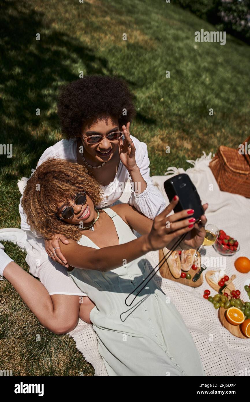 vue de dessus des amies afro-américaines surjoyées prenant selfie sur appareil photo vintage, pique-nique d'été Banque D'Images