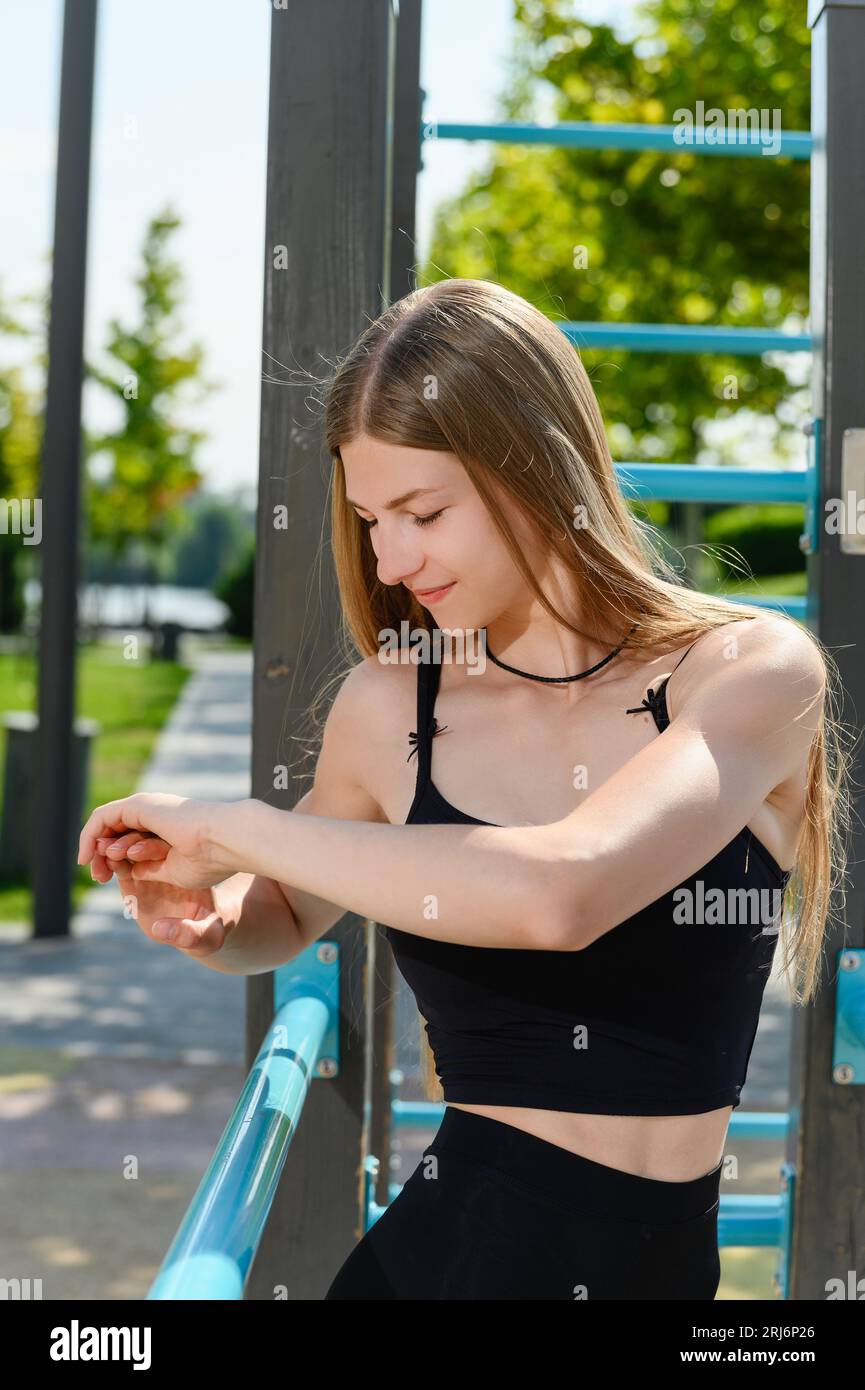 Une jeune fille en vêtements de sport se réchauffe sur un terrain de sport de rue avec des barres horizontales. Banque D'Images
