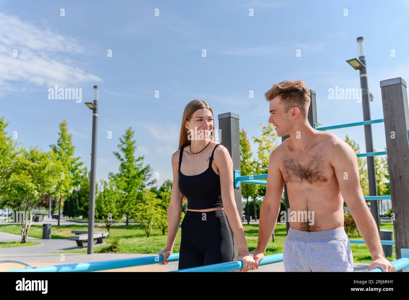Jeune couple attrayant faisant des pompes sur les barres inégales au terrain de sport en plein air. Banque D'Images