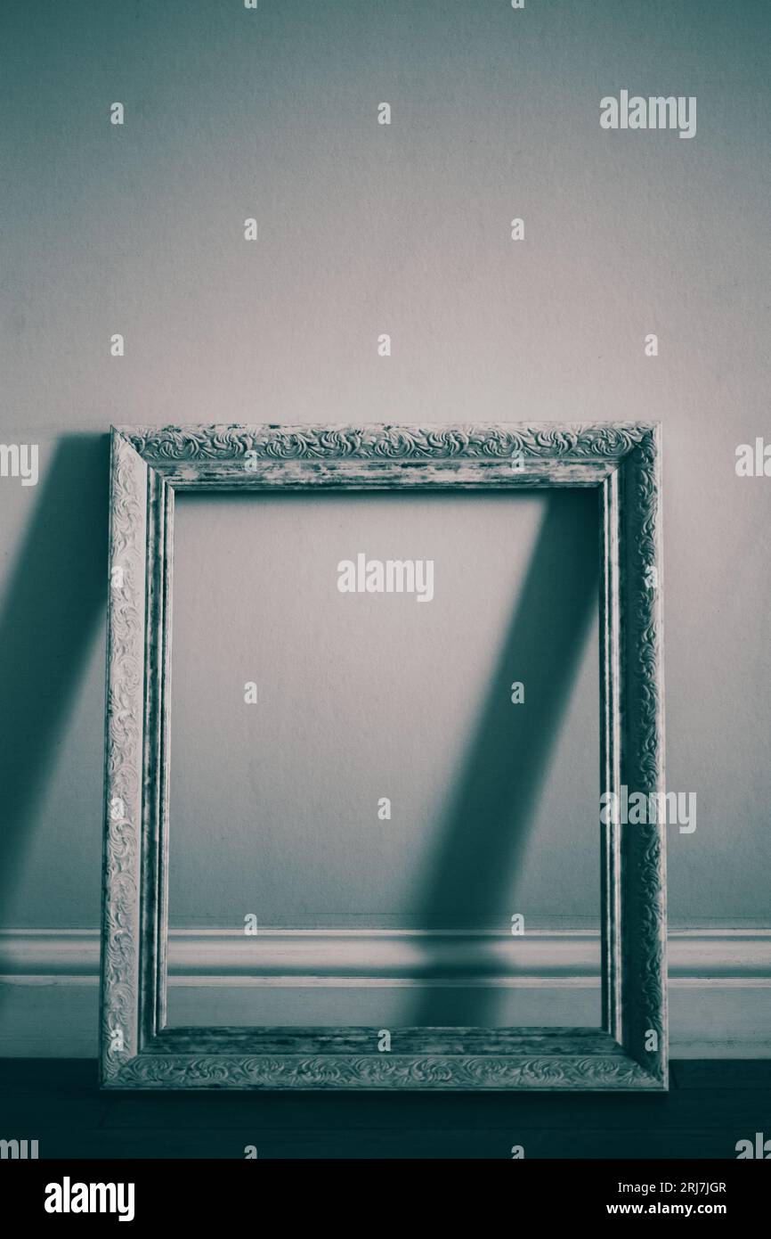 Une image faiblement éclairée d'un cadre vide blanc et magnifique debout contre un mur vide dans une galerie. Une préparation pour une exposition à venir, sans aucun Banque D'Images