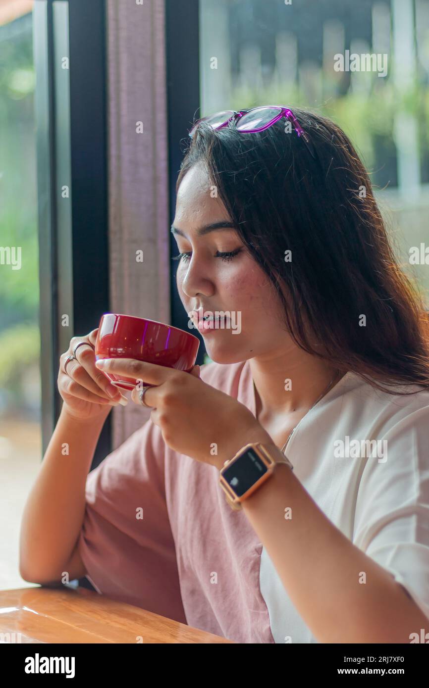 jeune femme asiatique tenant une tasse de café et pause. Belle jeune femme d'affaires asiatique dans le café, en utilisant un ordinateur portable et boire du café, souriant Banque D'Images