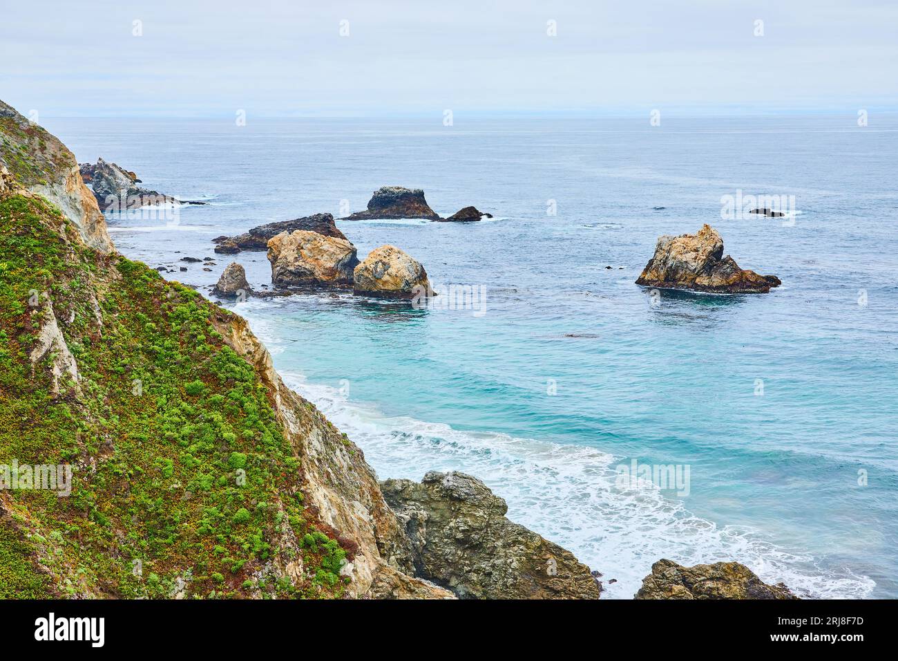 Vue panoramique de la falaise verte avec des vagues sarcelle qui s'écrasent contre des rochers et des rochers partiellement submergés Banque D'Images