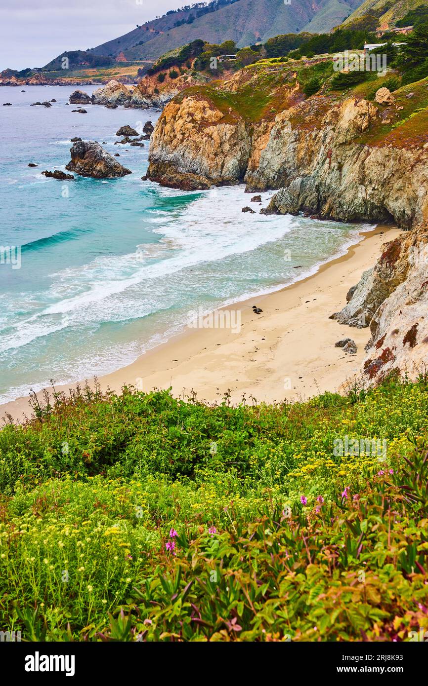 Magnifique colline verdoyante menant à une crique de sable avec des vagues qui s'écrasent et une colline lointaine falaise Banque D'Images