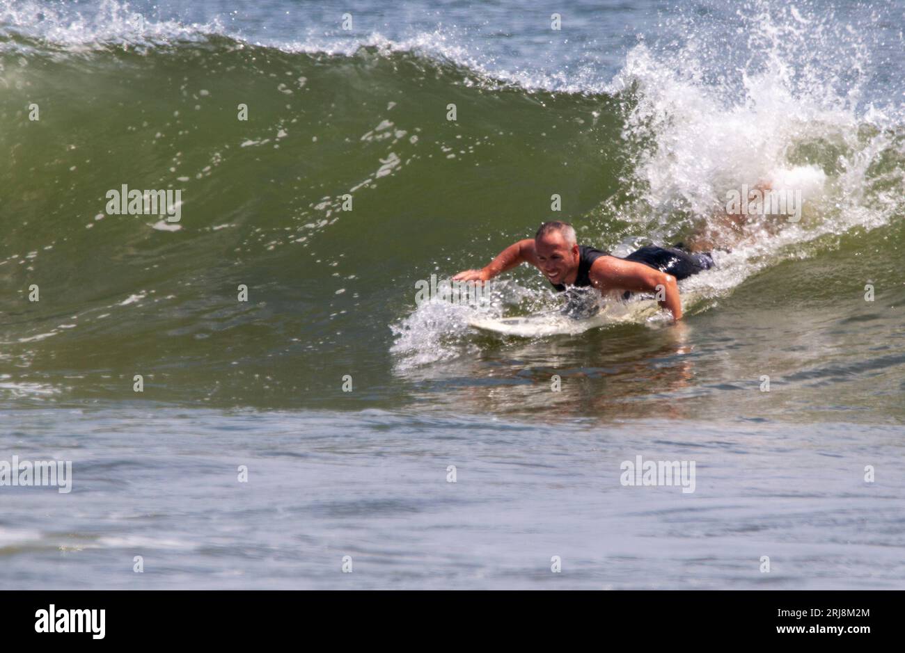 Gilgo Beach, New York, États-Unis - 22 juillet 2023 : un surfeur travaillant dur pour attraper une grande vague au début de sa balade dans l'océan avec un espace de copie sur TH Banque D'Images