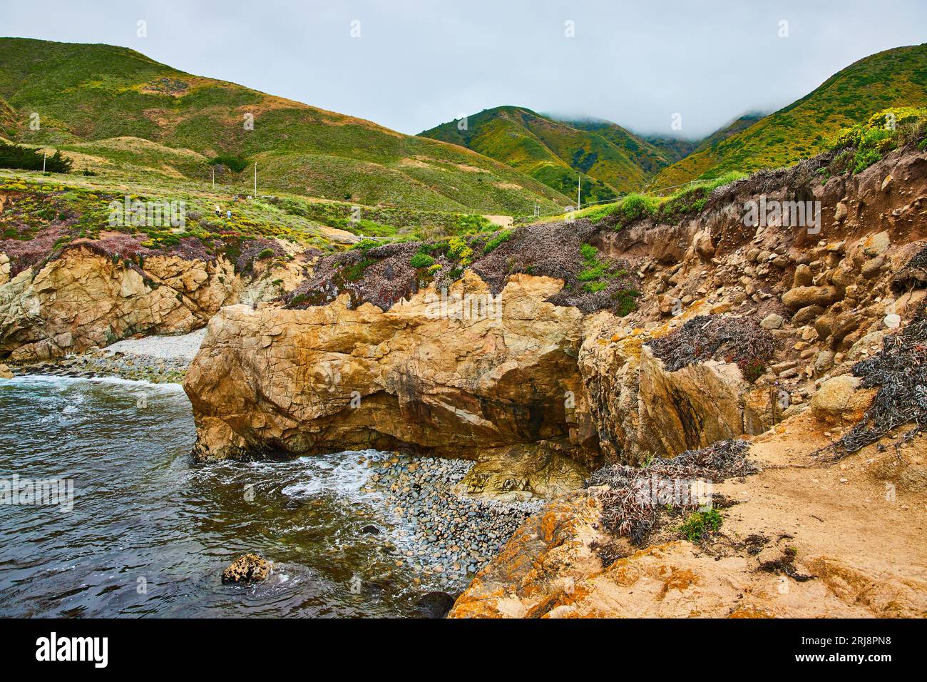 Rivage rocheux avec face de falaise et montagnes verdoyantes et vallonnées se terminant en nuages Banque D'Images