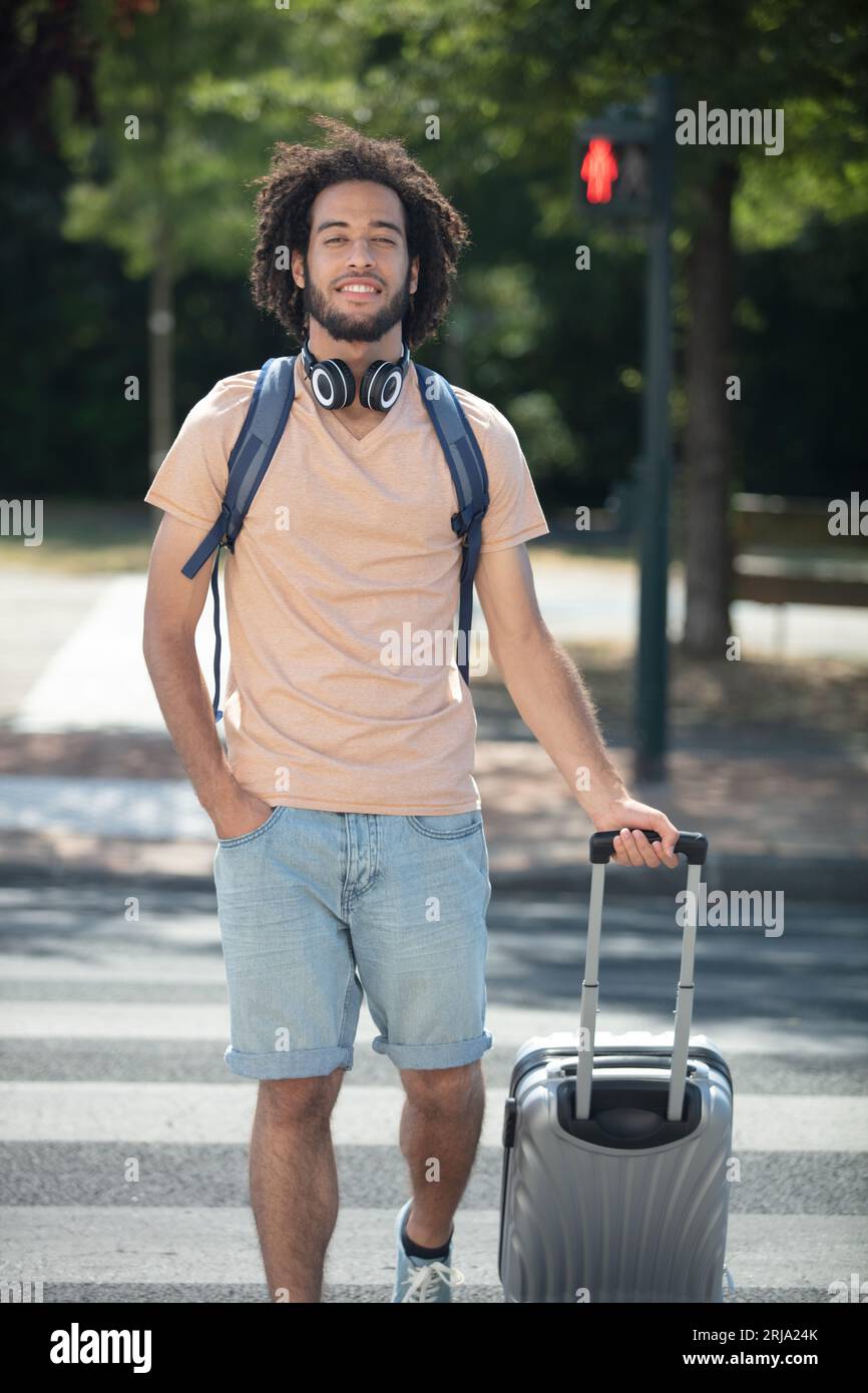 jeune bel homme traversant la rue avec sa valise Banque D'Images