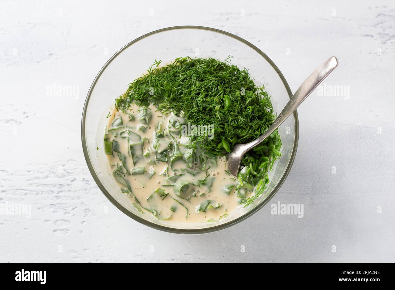 Bol en verre avec épinards et pâte à tarte aux herbes, épinards, oignon vert et aneth ajoutés au mélange oeuf-yogourt sur un fond bleu clair, vue de dessus. Pâte Banque D'Images
