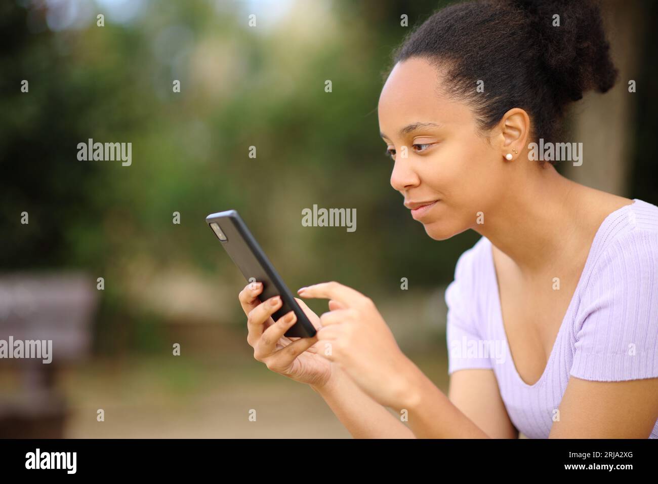 Profil d'une femme noire utilisant un téléphone intelligent assis dans un parc Banque D'Images
