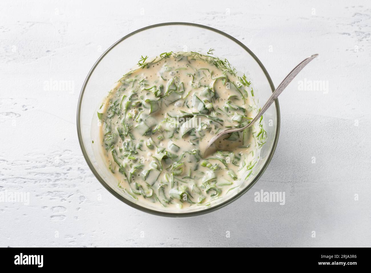 Bol en verre avec pâte à tarte, avec épinards et herbes sur un fond bleu clair, vue de dessus. Pétrissage de la pâte, étape de cuisson. Banque D'Images