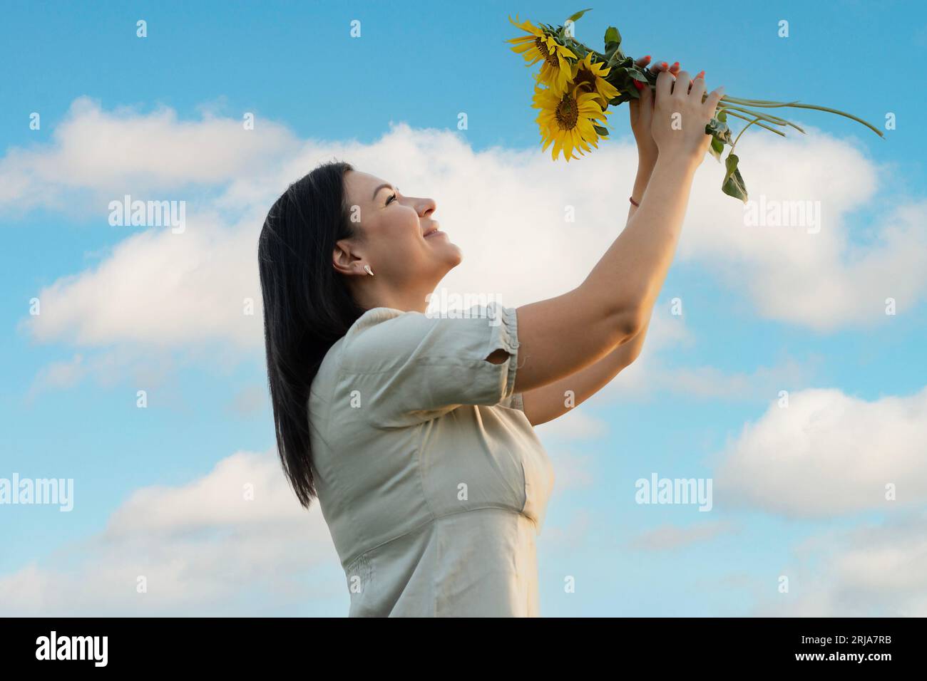 Un symbole de paix. Une belle et heureuse fille caucasienne se tient contre le ciel bleu et tient un bouquet de fleurs avec des tournesols jaunes dans ses mains Banque D'Images