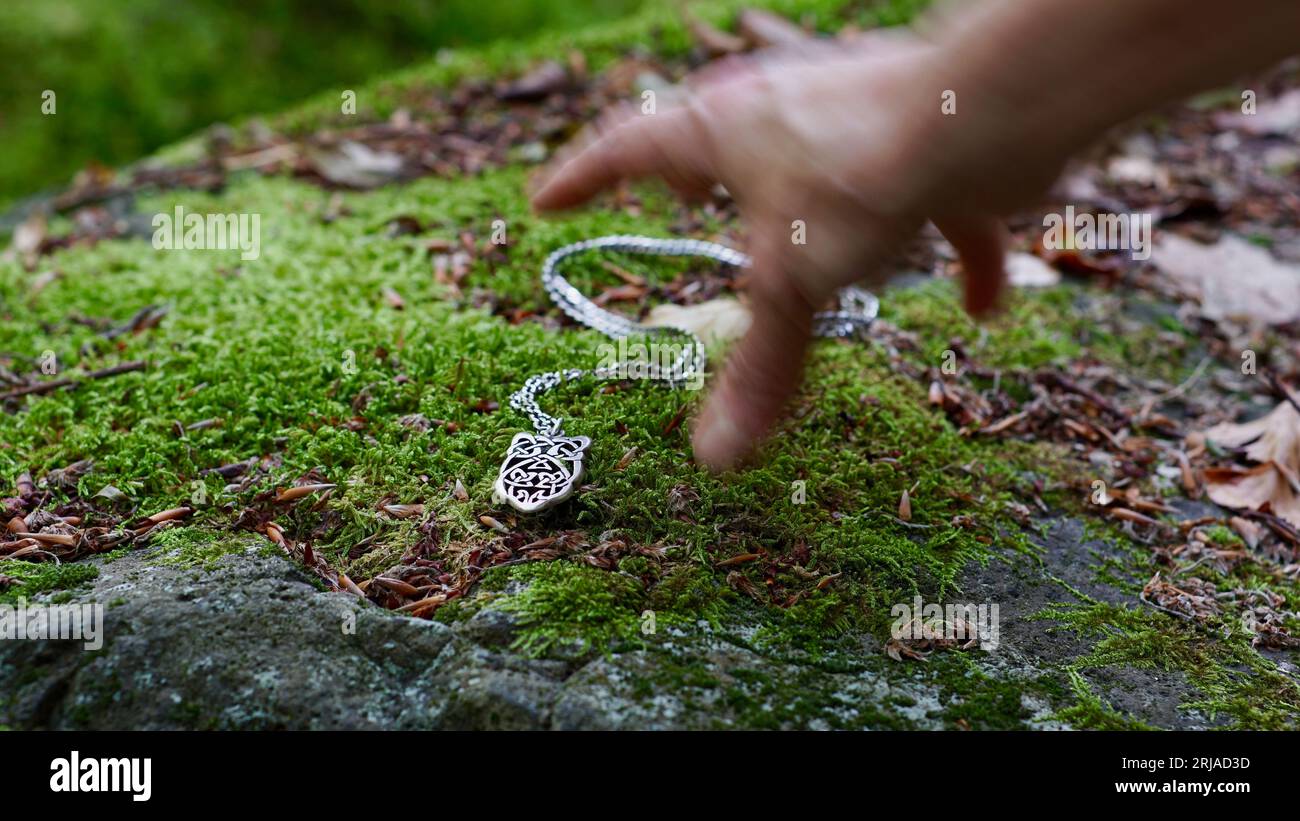 Une main de femme tendant vers un collier d'argent couché sur une pierre mousseline. Banque D'Images