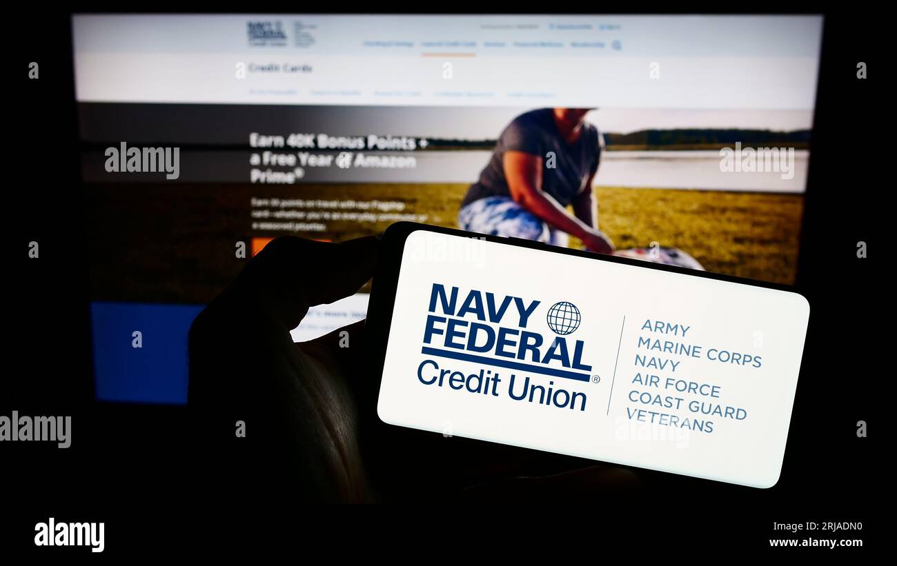 Personne tenant le téléphone portable avec le logo de l'institution financière Navy Federal Credit Union sur l'écran en face de la page Web. Concentrez-vous sur l'affichage du téléphone. Banque D'Images